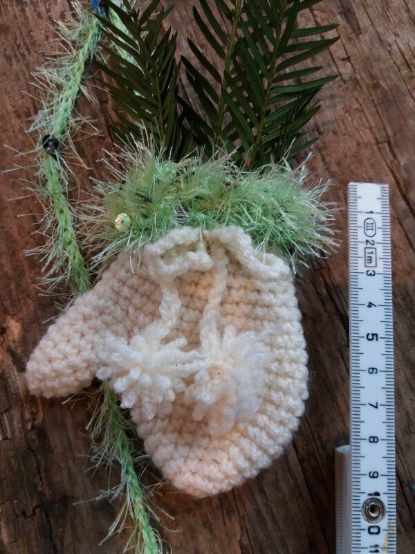 Kleiner gehäkelter Beutel mit Kordelzug, Bommelverzierungen, grünem Effektrand und Lineal zur Größenanzeige