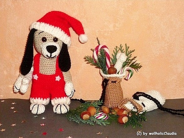 Gehäkelter Amigurumi-Hund mit roter Nikolausmütze und Strampelhose neben Tannengrün, Zuckerstangen und kleinem Säckchen
