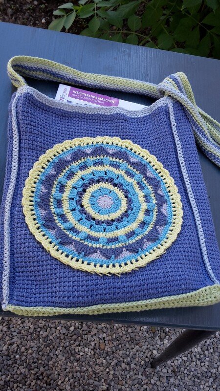 Gehäkelte lila Tasche mit rundem Mandala-Motiv in Gelb, Blau und Violett auf der Vorderseite