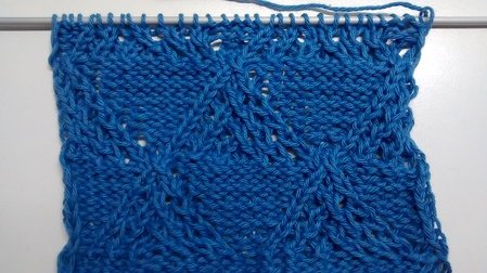 Blaue gestrickte Probe mit Rautenmuster und Lochreihen auf Nadel