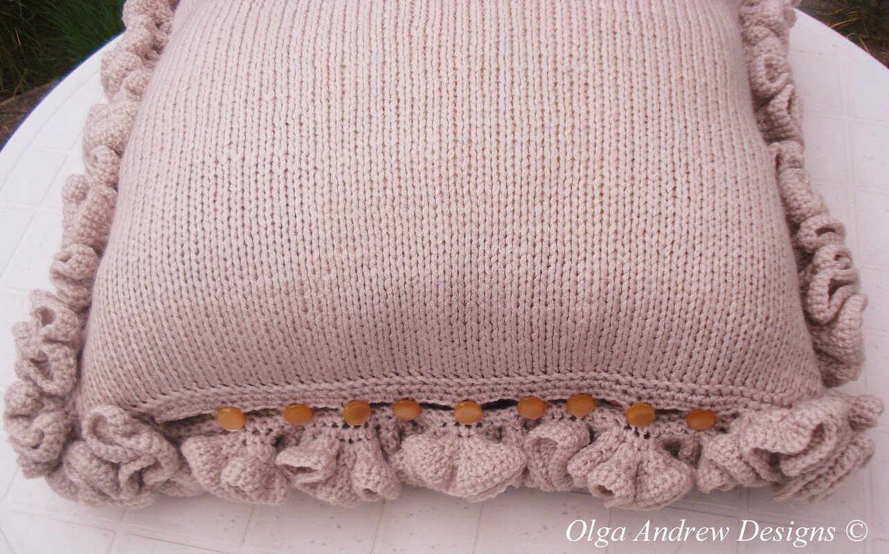 Light beige knitted square pillow with ruffled edges and wooden bead trim