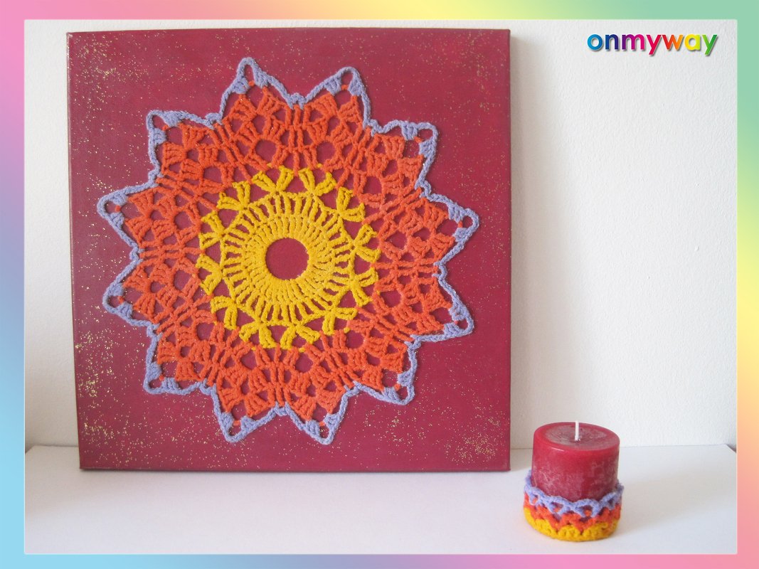 Rote Leinwand mit gehäkeltem Mandala in Gelb, Orange und Lila; rote Kerze mit Häkelüberzug.