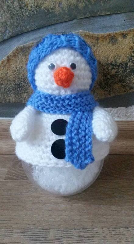 Gehäkelter Schneemann mit blauer Mütze und Schal, orangefarbene Nase, schwarze Knöpfe, sitzt auf Glasbehälter