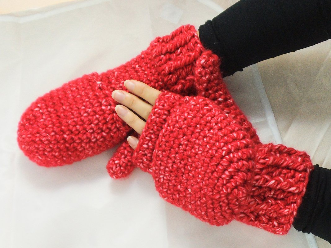 Rote gehäkelte Handschuhe mit weißer Sprenkelung, eine Hand fingerlos, die andere als Fäustling