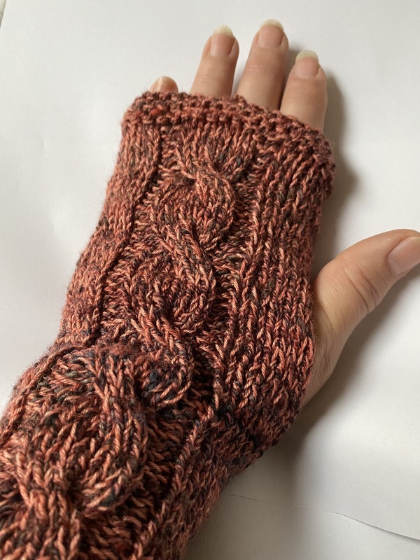 Gestrickte rostrote, fingerlose Armstulpe mit Zopfmuster an einer Hand