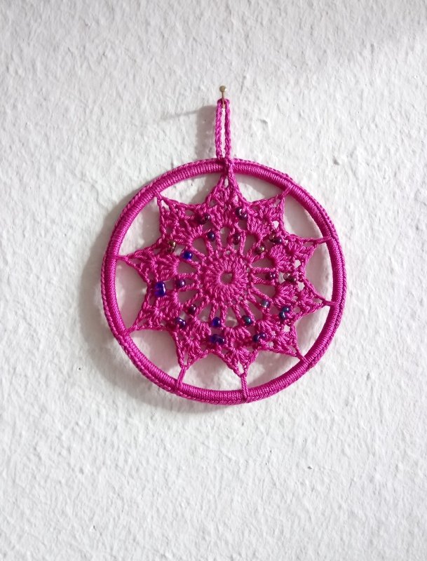 Gehäkelter Stern in Fuchsia mit Perlen an weißer Wand