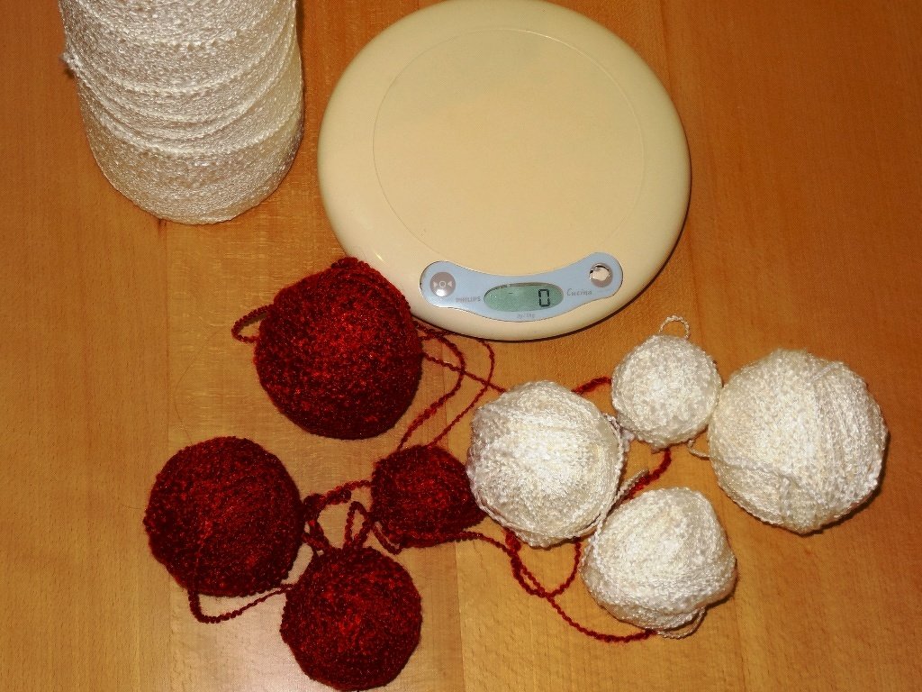 Rote und weiße Garnknäuel, eine Garnspule und eine digitale Waage auf einem Holztisch.