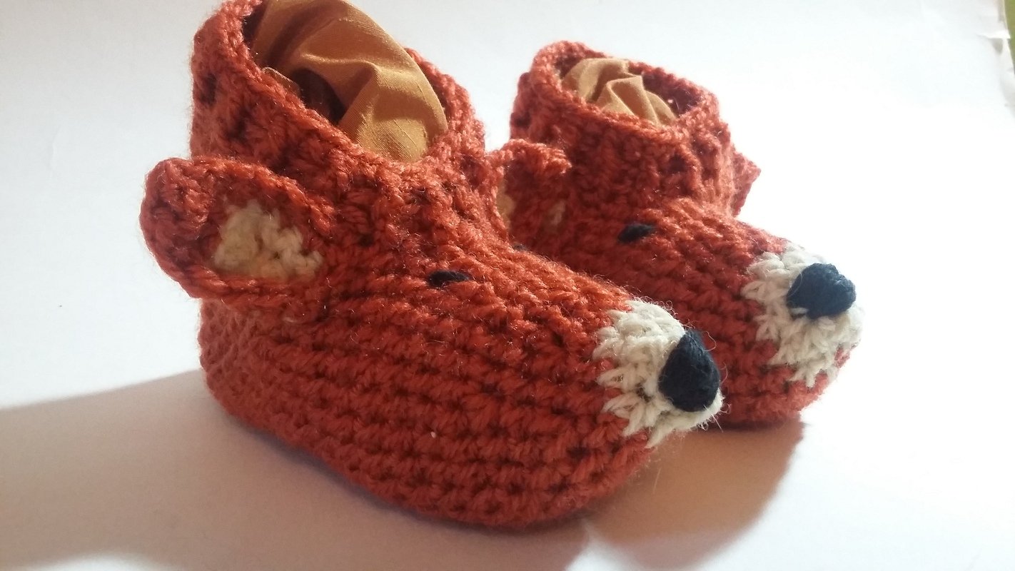 Detailansicht von zwei gehäkelten Baby-Babyschuhen in Orange mit weißen Schnauzen und schwarzen Nasen