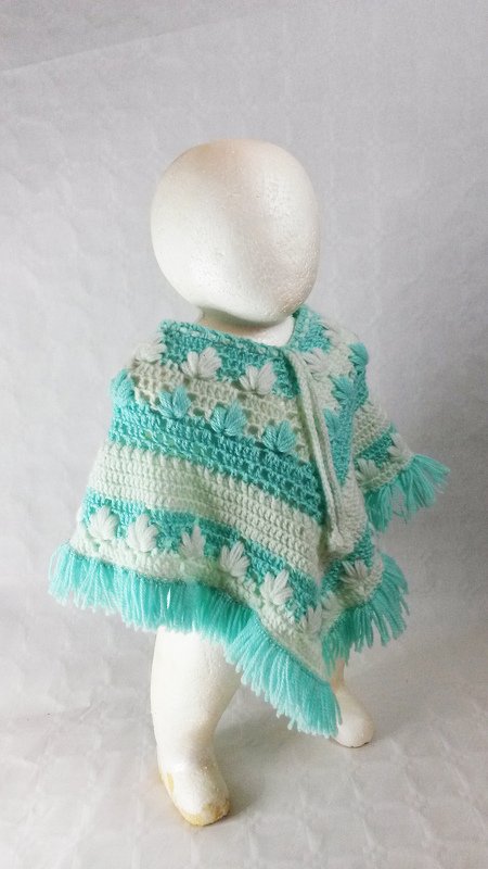 Gehäkelter Poncho in Türkis und Weiß mit erhabenen Blüten, Bindeband am Hals und Fransen.