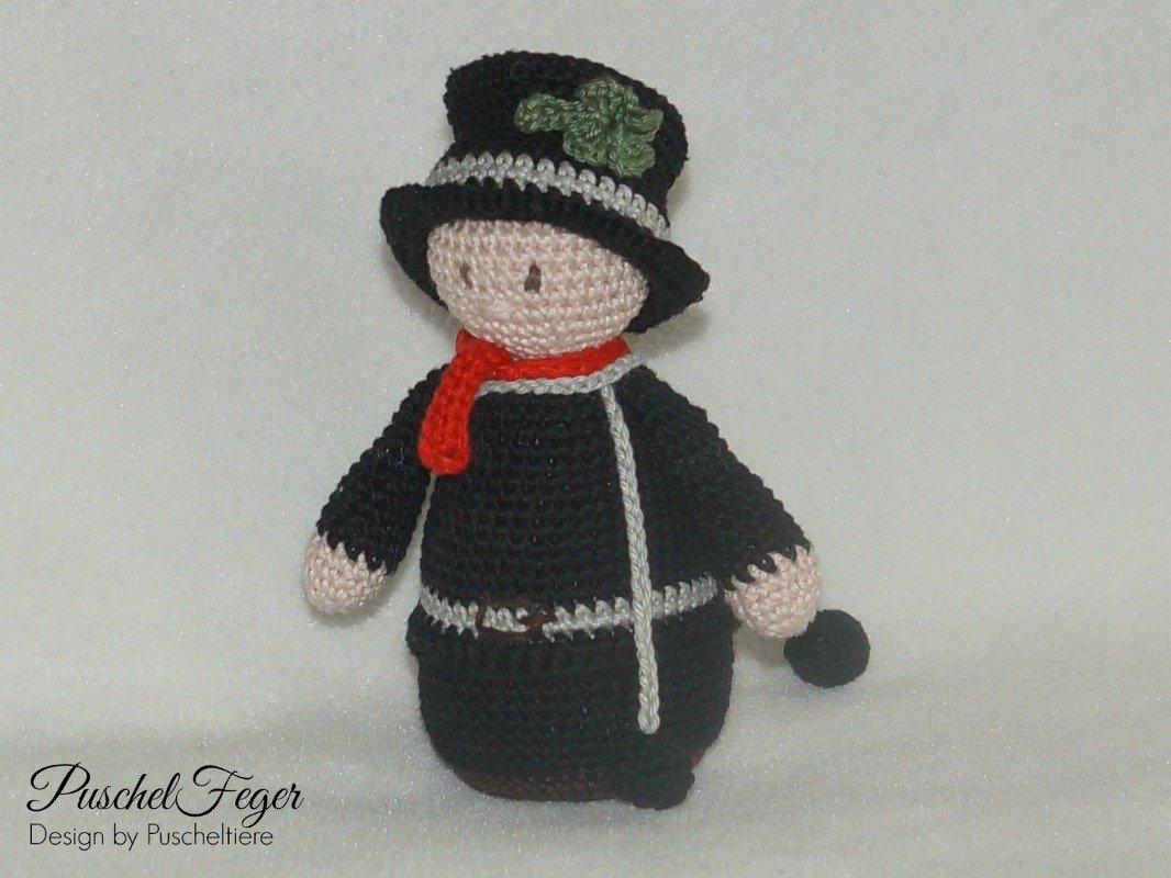 Gehäkelte Schornsteinfeger-Puppe in Schwarz mit rotem Schal, schwarzem Zylinder mit grünem Kleeblatt und kleinem Besen.