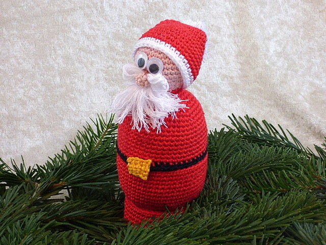 Gehäkelter Weihnachtsmann mit roter Mütze, Fransenbart und Wackelaugen auf Tannenzweigen