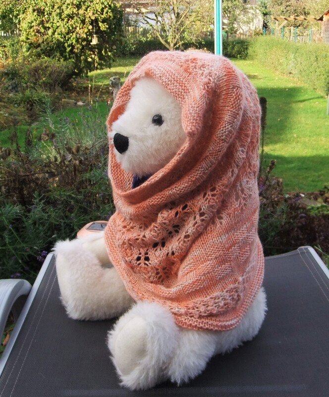 Nahaufnahme eines pfirsichfarbenen gestrickten Loops mit Ajourmuster an einem Teddybär