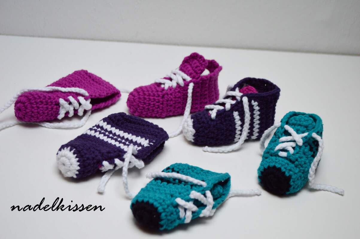 Gehäkelte Babysneaker in Pink, Violett und Türkis mit weißen Schnürsenkeln auf weißem Hintergrund