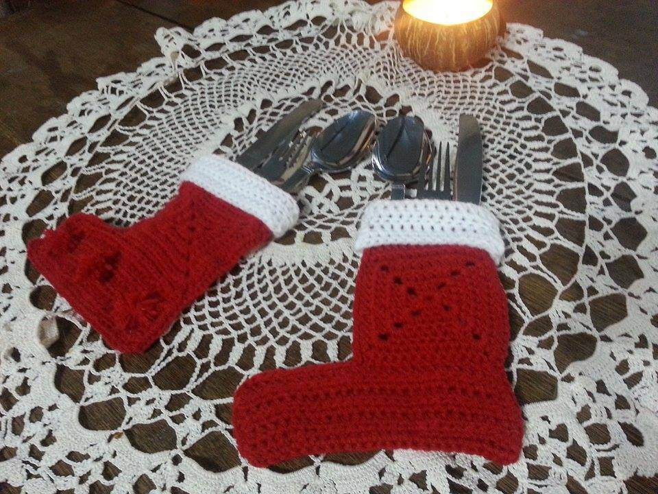 Zwei rote, gehäkelte Nikolausstiefel mit weißem Bündchen als Besteckhalter auf einer weißen Spitzendecke