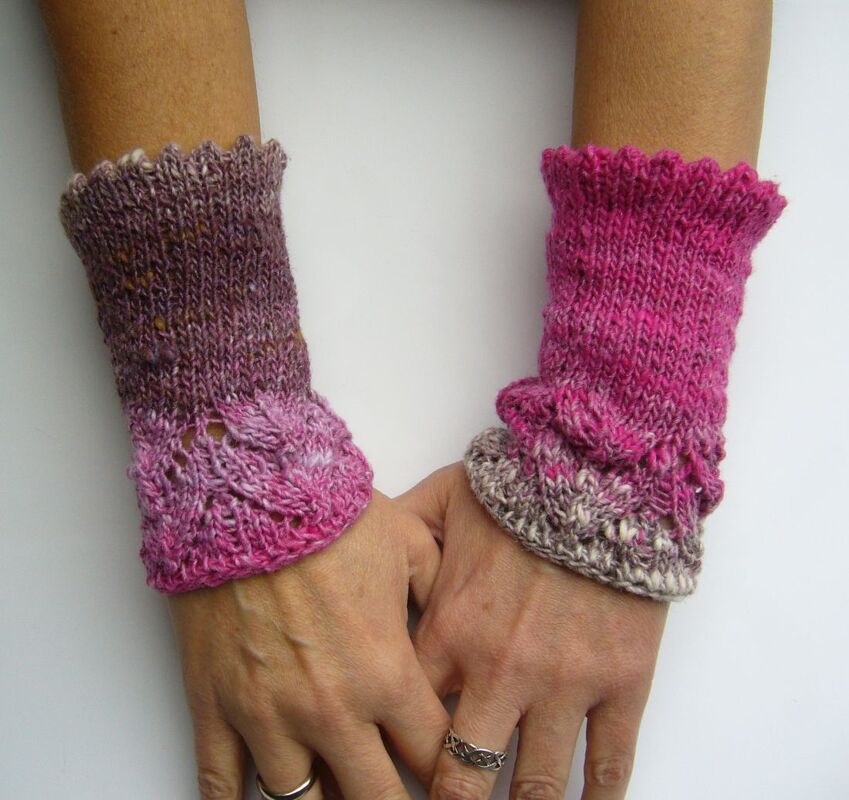 Nahaufnahme kurzer handgestrickter Armstulpen mit gewelltem Bündchen und Lochmuster im Farbverlauf.