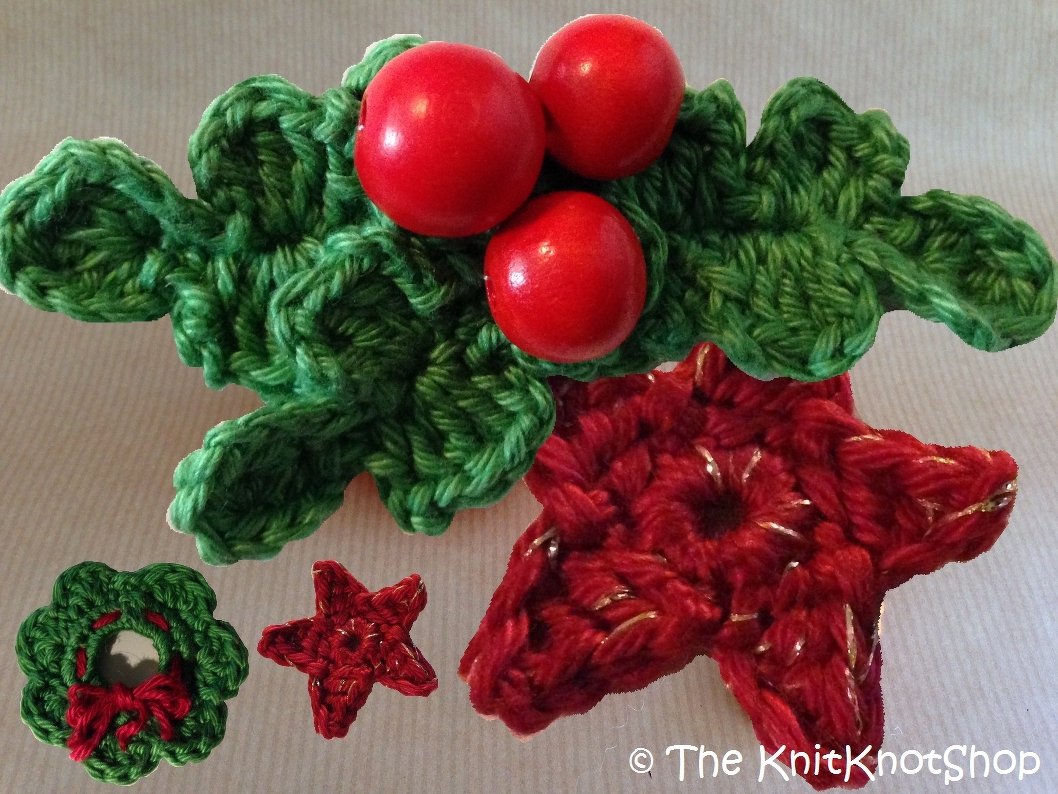 Gehäkelte Weihnachtsapplikationen: grüner Stechpalmenzweig mit drei roten Kugeln, kleiner Kranz mit roter Schleife und zwei rote Sterne mit goldenen Akzenten auf hellem Hintergrund
