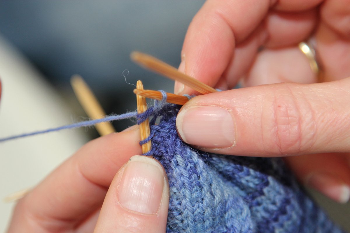 Detailaufnahme: Hände beim Stricken einer blau melierten Kindersocke mit Nadelspiel