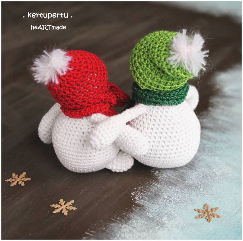 Rückansicht zweier gehäkelter Amigurumi‑Schneemänner mit roten und grünen Mützen, Arm in Arm