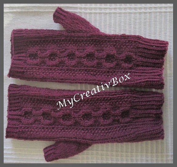 Zwei violett-bordeauxfarbene gestrickte Armstulpen mit Zopfmuster und Daumenloch auf hellem Untergrund