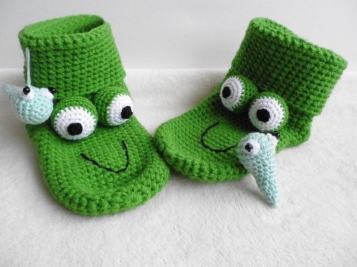Grüne gehäkelte Hausschuhe mit großen Augen-Applikationen und kleinen Kaulquappen-Anhängern