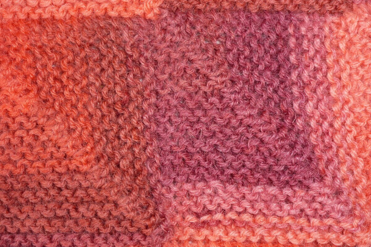 Nahaufnahme eines gestrickten Schals in orange-rosa Farbverlauf mit kraus-rechter Maschenstruktur