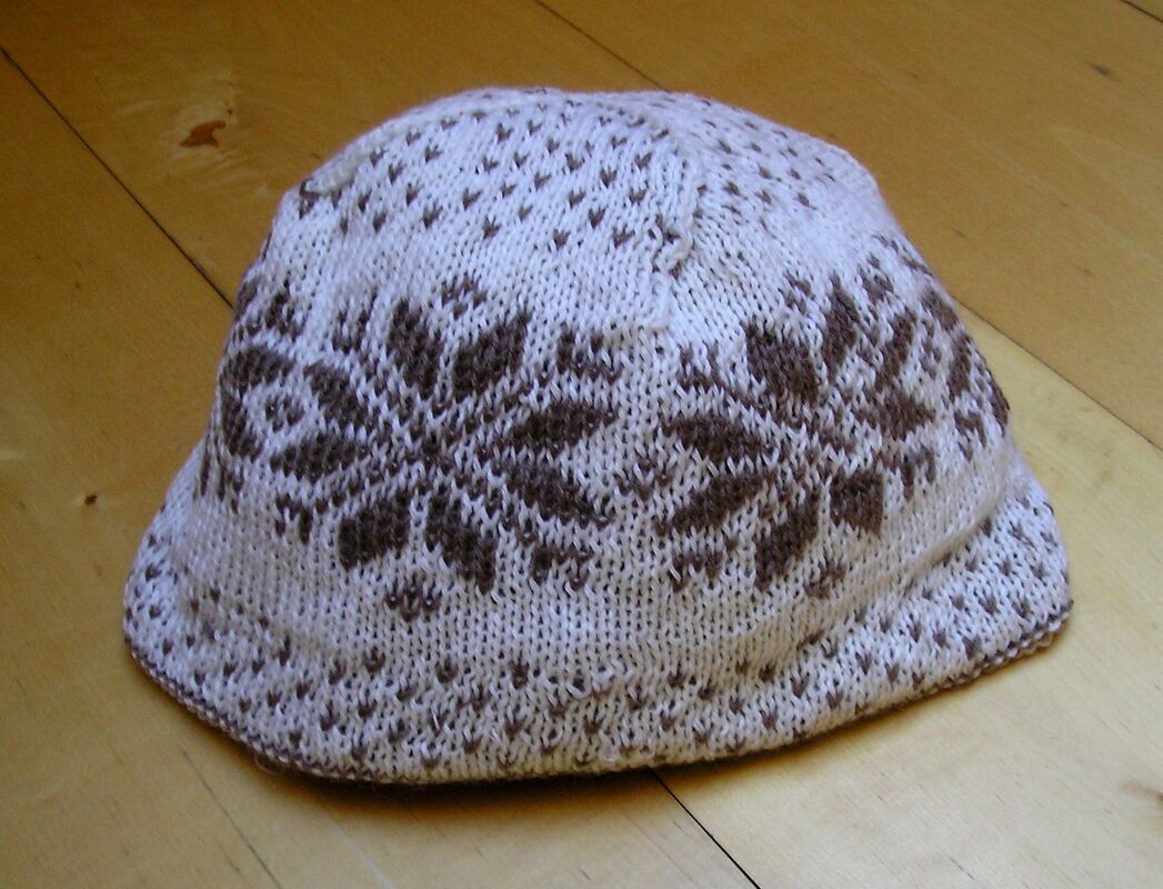 Gestrickte Mütze in Weiß und Braun mit symmetrischem Schneeflockenmuster auf hellem Holz