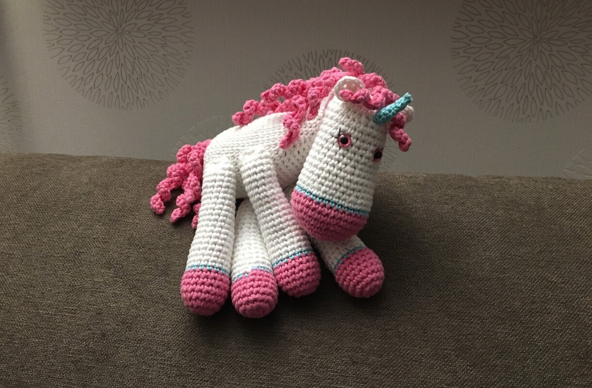 Abbildung eines gehäkelten Einhorn-Amigurumis mit rosa Hufen, weißem Körper und türkisfarbenem Horn