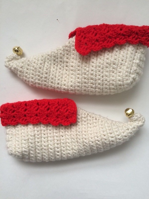 Pair of white crochet elf slippers with red scalloped cuffs and small gold bells on curled toes