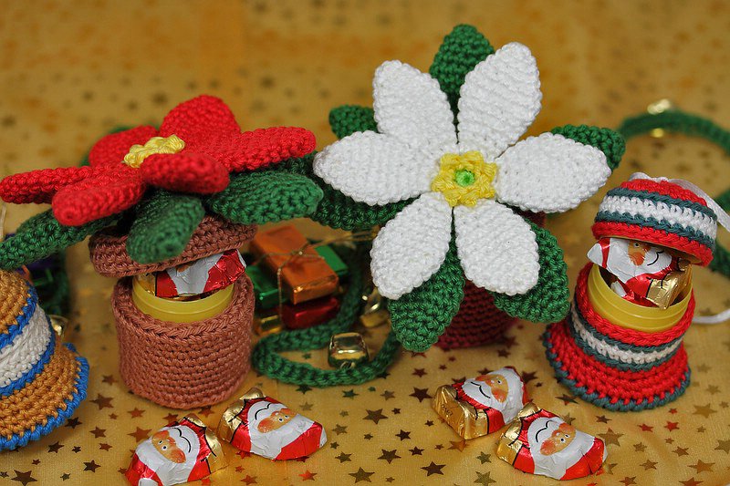 Weiße und rote gehäkelte Blüten mit kleinen Häkelüberzügen und Schoko-Nikoläusen auf goldenem Sternenstoff