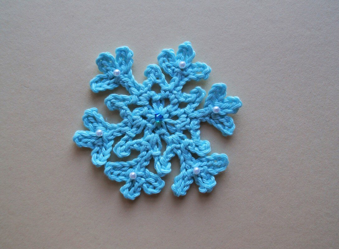 Nahaufnahme einer hellblauen Häkel-Schneeflocke mit Perlenverzierung