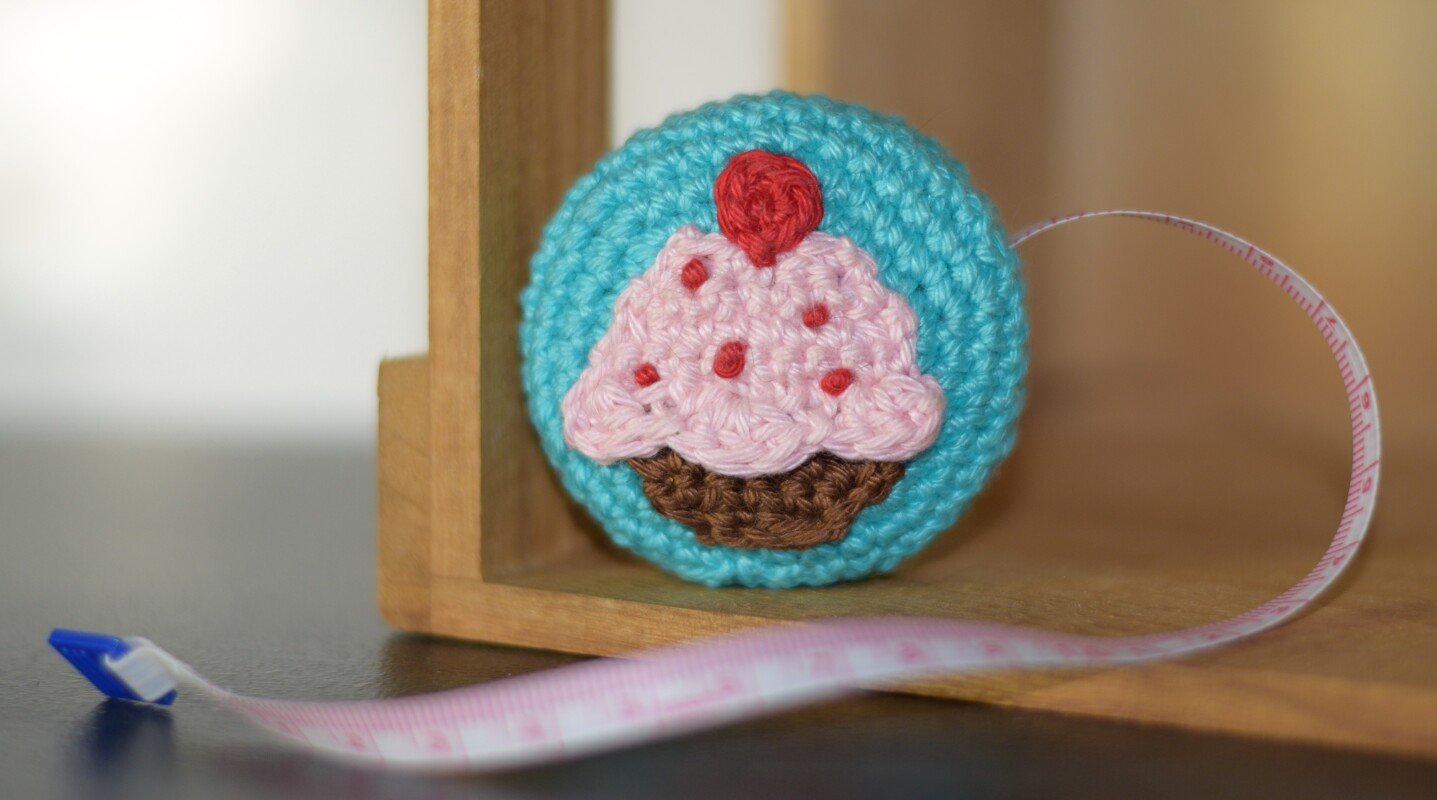 Rundes gehäkeltes Maßband mit türkiser Hülle und rosa Cupcake-Applikation
