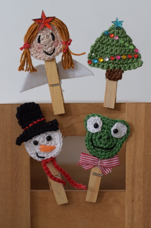Vier gehäkelte Wäscheklammer‑Figuren: Engel, Weihnachtsbaum, Schneemann und Frosch an Holzwäscheklammern.