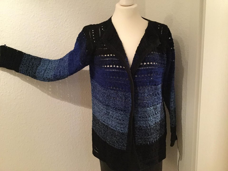 Gehäkelte Langjacke mit Farbverlauf von Blau zu Schwarz an einer Schneiderpuppe, ein Ärmel ausgestreckt