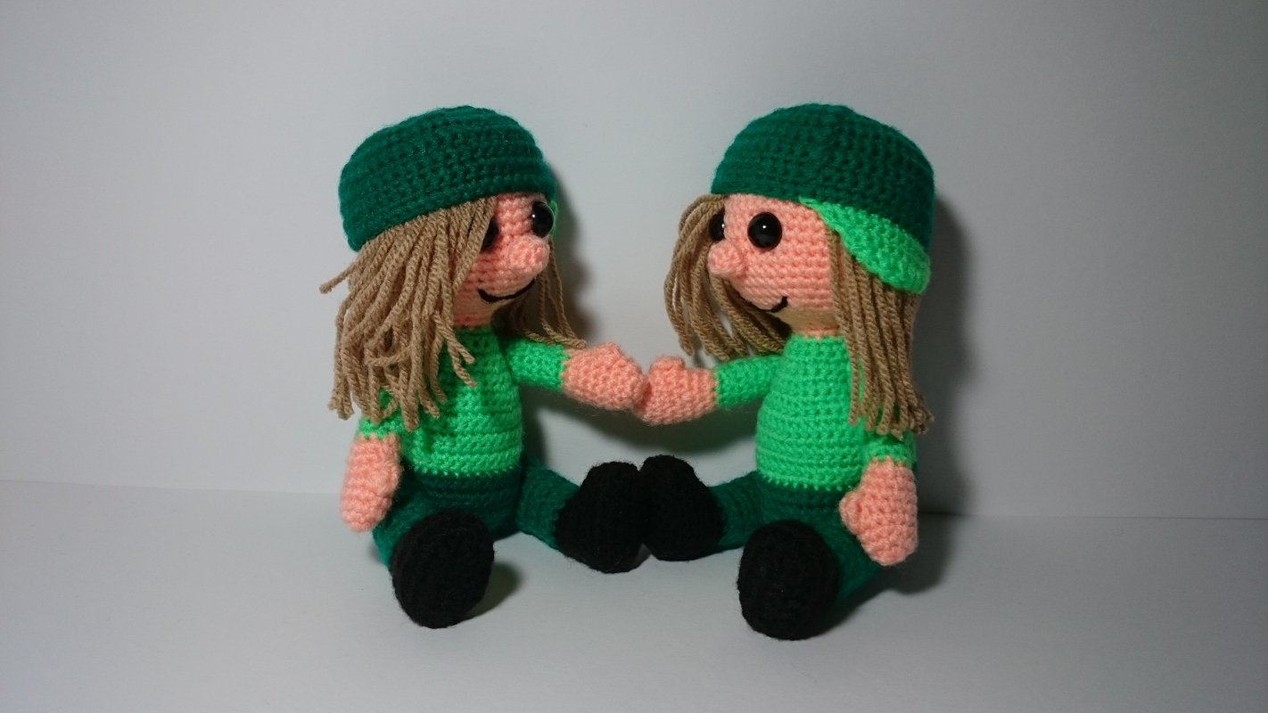 Zwei gehäkelte Amigurumi-Puppen in grüner Kleidung, die Händchen halten
