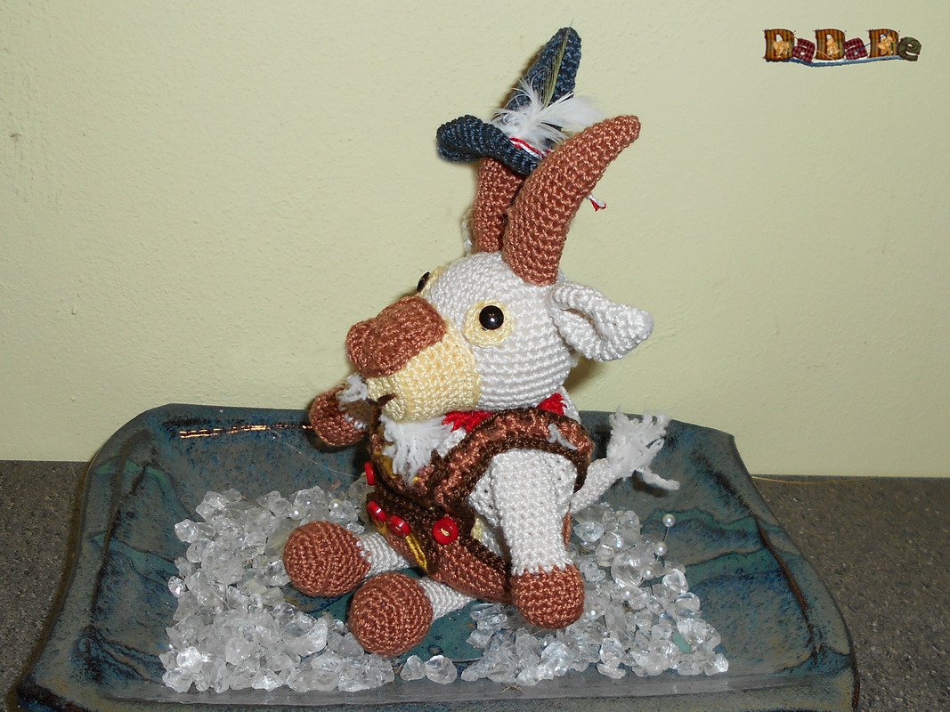 Gehäkelte Amigurumi-Ziege mit braunen Hörnern und dunkelblauem Hut in blauer Schale
