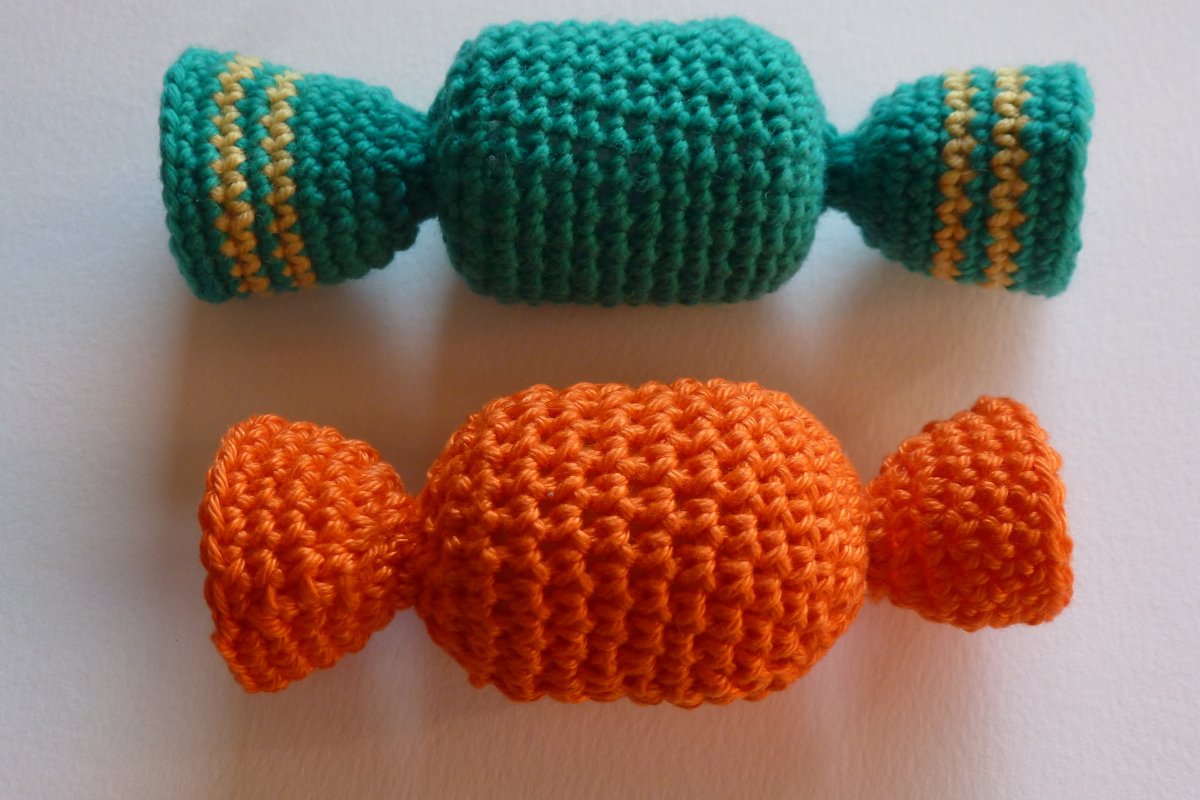 Zwei gehäkelte Katzenspielzeuge in Bonbonform, grün mit gelben Streifen und orange