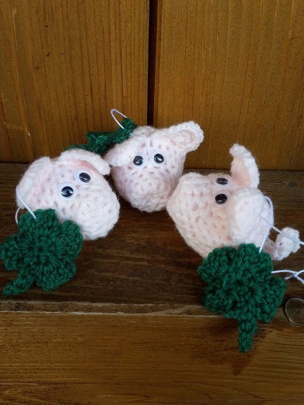 Drei handgehäkelte rosa Schweinchen-Amigurumi mit kleinen grünen Kleeblättern
