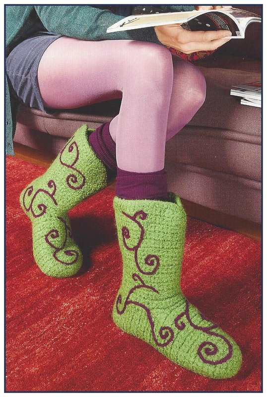 Gehäkelte grüne Filzstiefel mit lila Ornamenten an den Füßen einer sitzenden Person