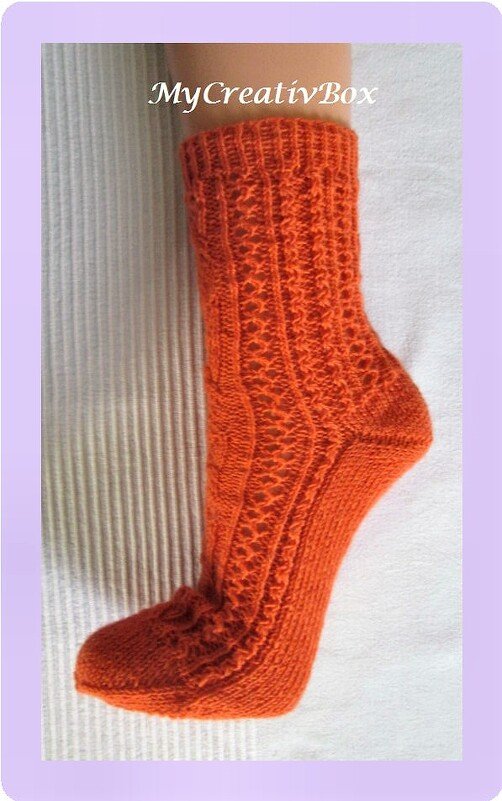 Wadenhohe orangefarbene, gestrickte Socke mit Rippbündchen, Zopfmotiv und Lochmuster auf hellem Untergrund