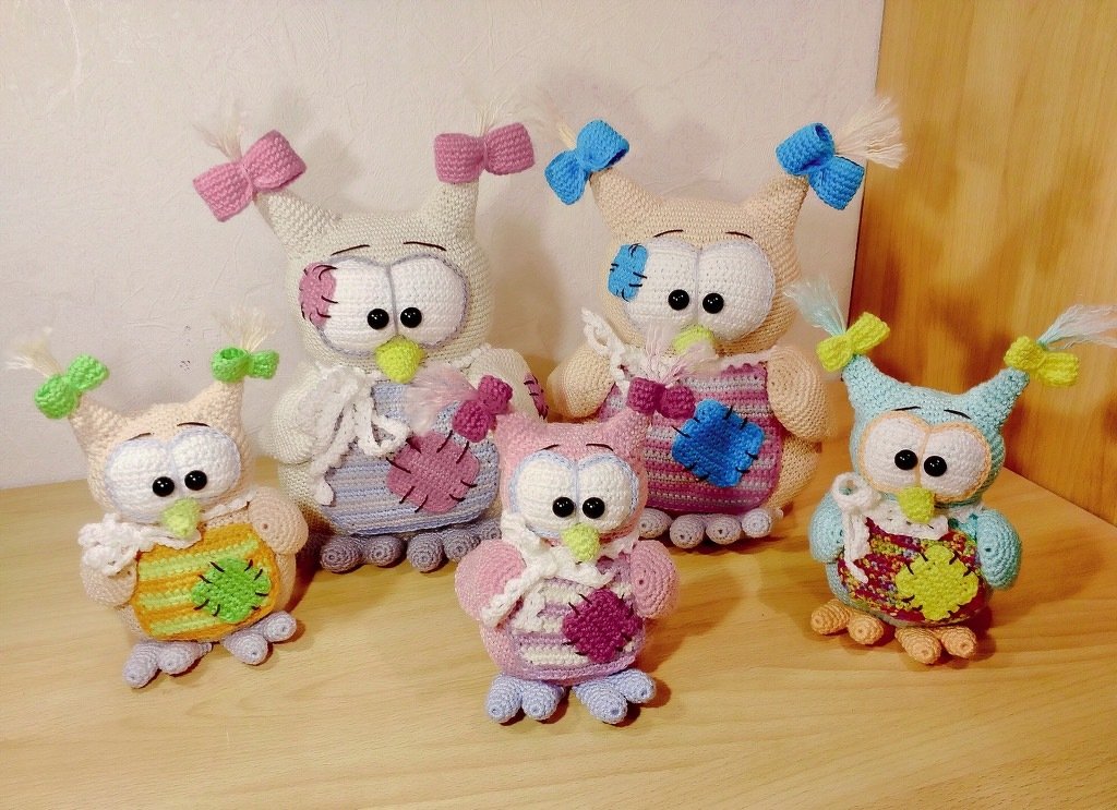 Fünf gehäkelte Amigurumi‑Eulen in verschiedenen Größen mit Schleifen und aufgestickten Flicken am Bauch.