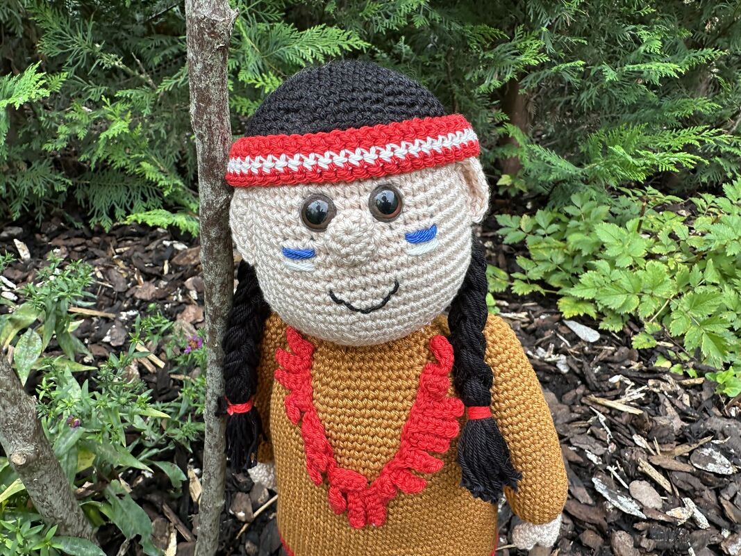 Gehäkelte Amigurumi-Puppe mit schwarzen Zöpfen, rot-weißem Stirnband, braunem Oberteil und rotem Halsschmuck