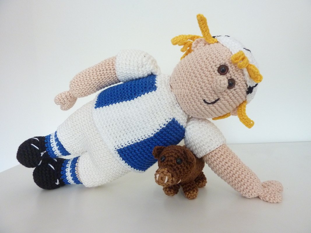 Gehäkelte Amigurumi-Puppe in weiß-blauem Trikot mit gelben Zöpfen und kleinem braunem Amigurumi-Tier