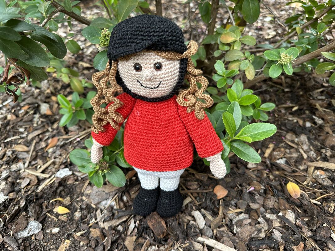 Gehäkelte Amigurumi-Reiterpuppe mit schwarzem Reithelm, rotem Oberteil, weißer Hose und schwarzen Stiefeln im Grünen