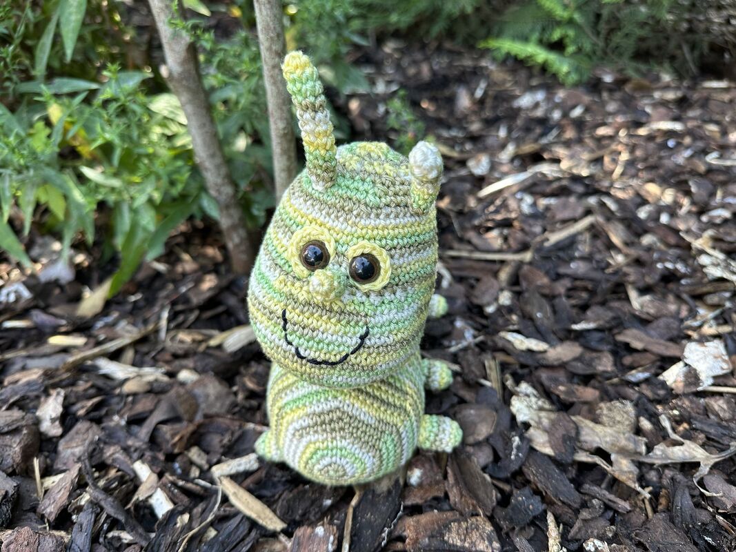 Gehäkelte grün-gelbe Amigurumi-Raupe aus Verlaufsgarn auf Rindenmulch