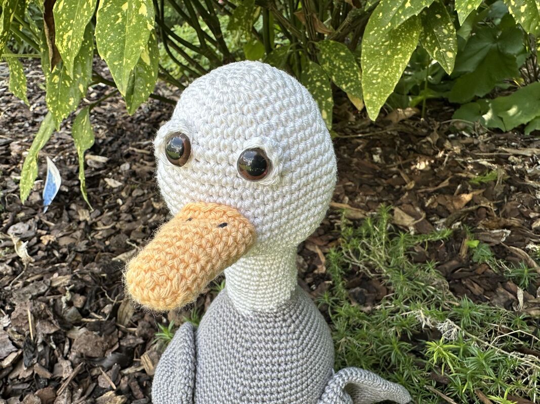 Gehäkelte Ente Amigurumi mit orangenem Schnabel und großen Sicherheitsaugen auf Rindenmulch