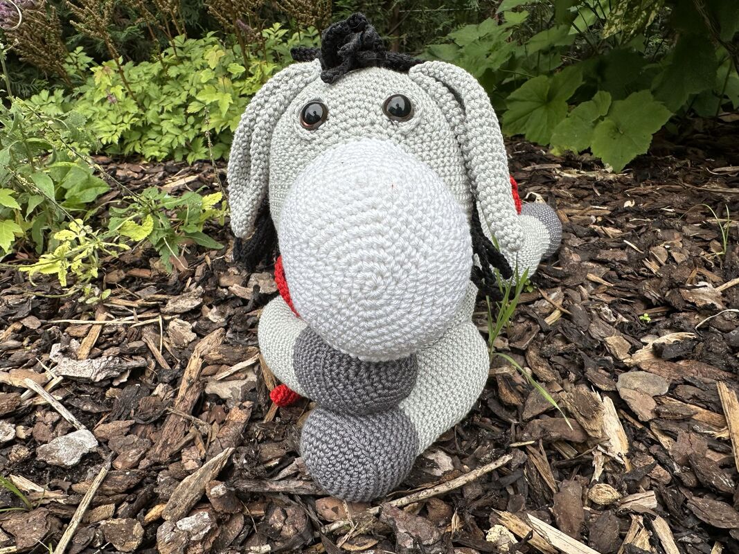 Gehäkelter Amigurumi-Esel in Grau und Weiß auf Rindenmulch