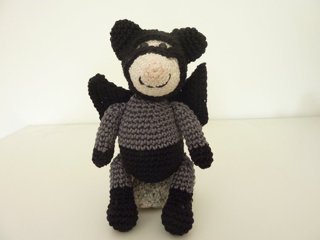 Vorderansicht eines gehäkelten Amigurumi mit Maske und Flügeln in Grau-Schwarz