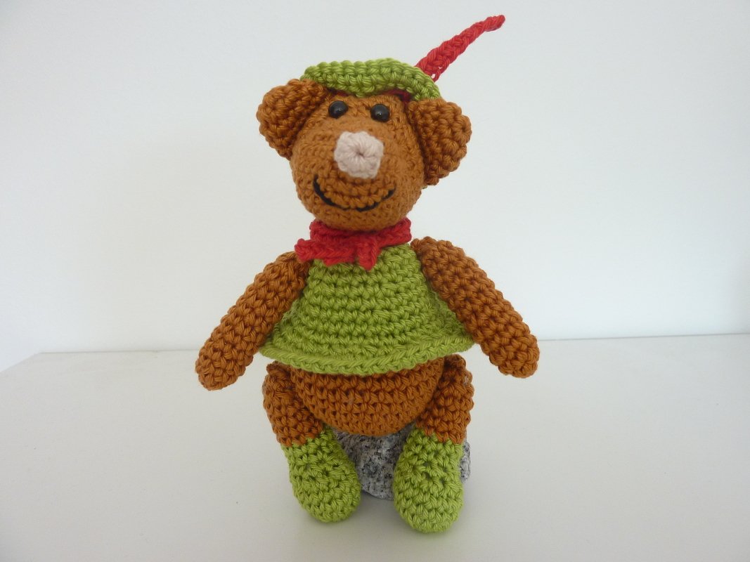 Gehäkelte braune Amigurumi-Maus mit grünem Oberteil, rotem Halstuch und grünem Hut mit roter Feder