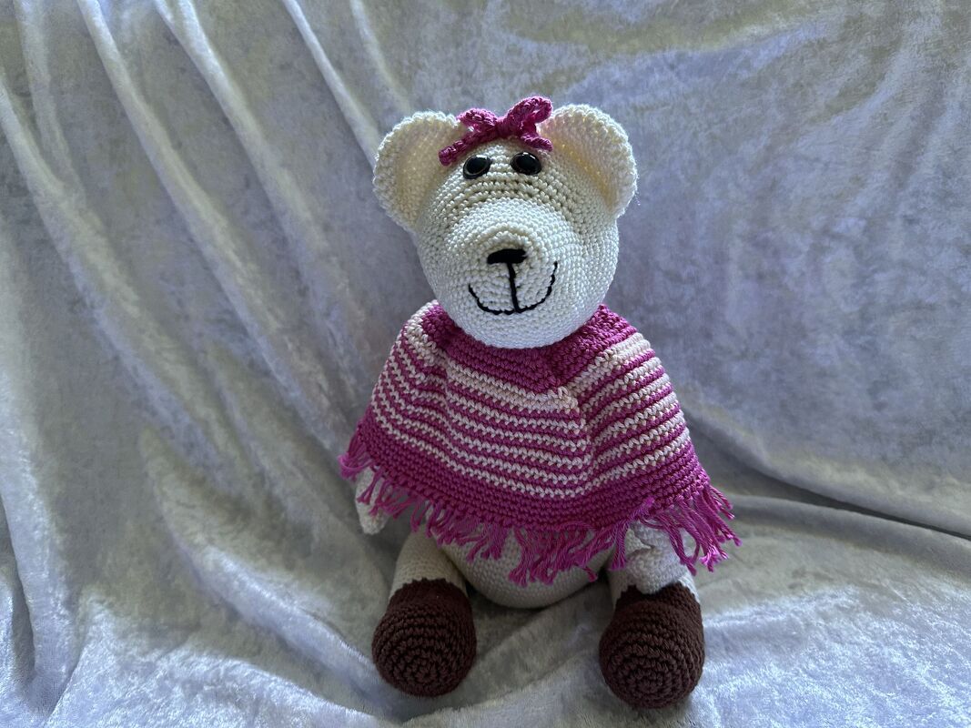 Weißer gehäkelter Teddybär mit pink-weiß gestreiftem Poncho und pinker Schleife
