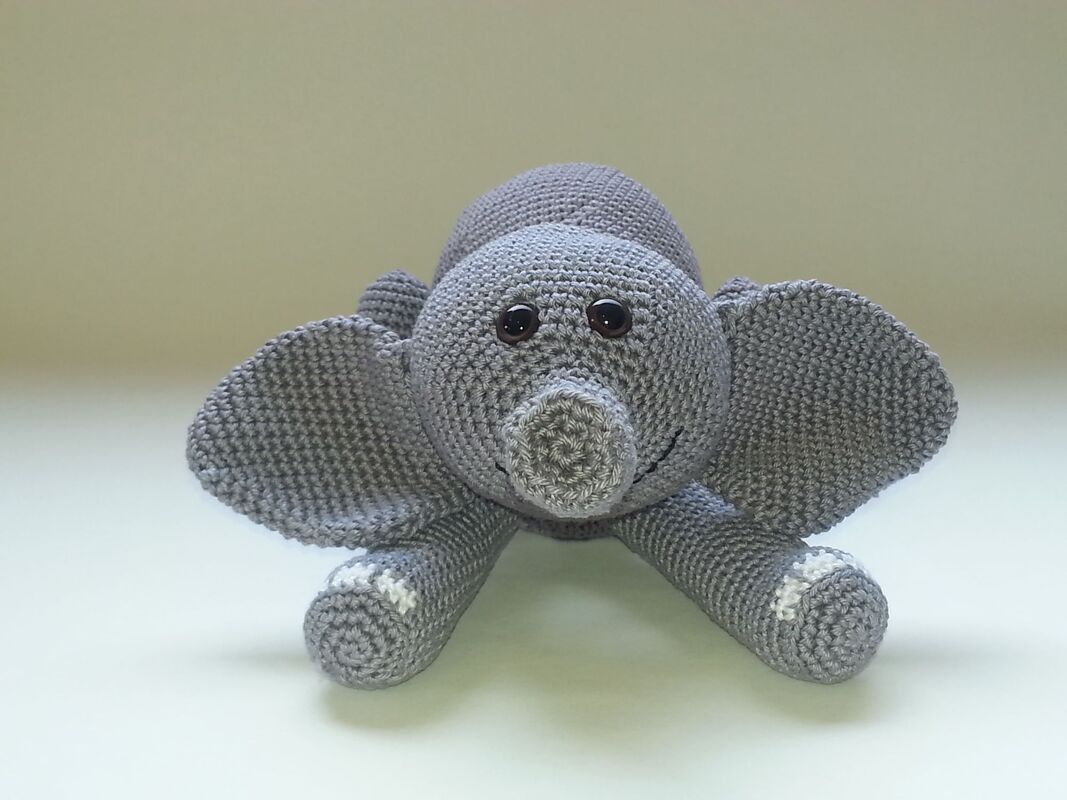 Vorderansicht eines grauen, gehäkelten Elefanten-Amigurumi mit erkennbaren Maschen und dunklen, runden Augen auf hellem Hintergrund.